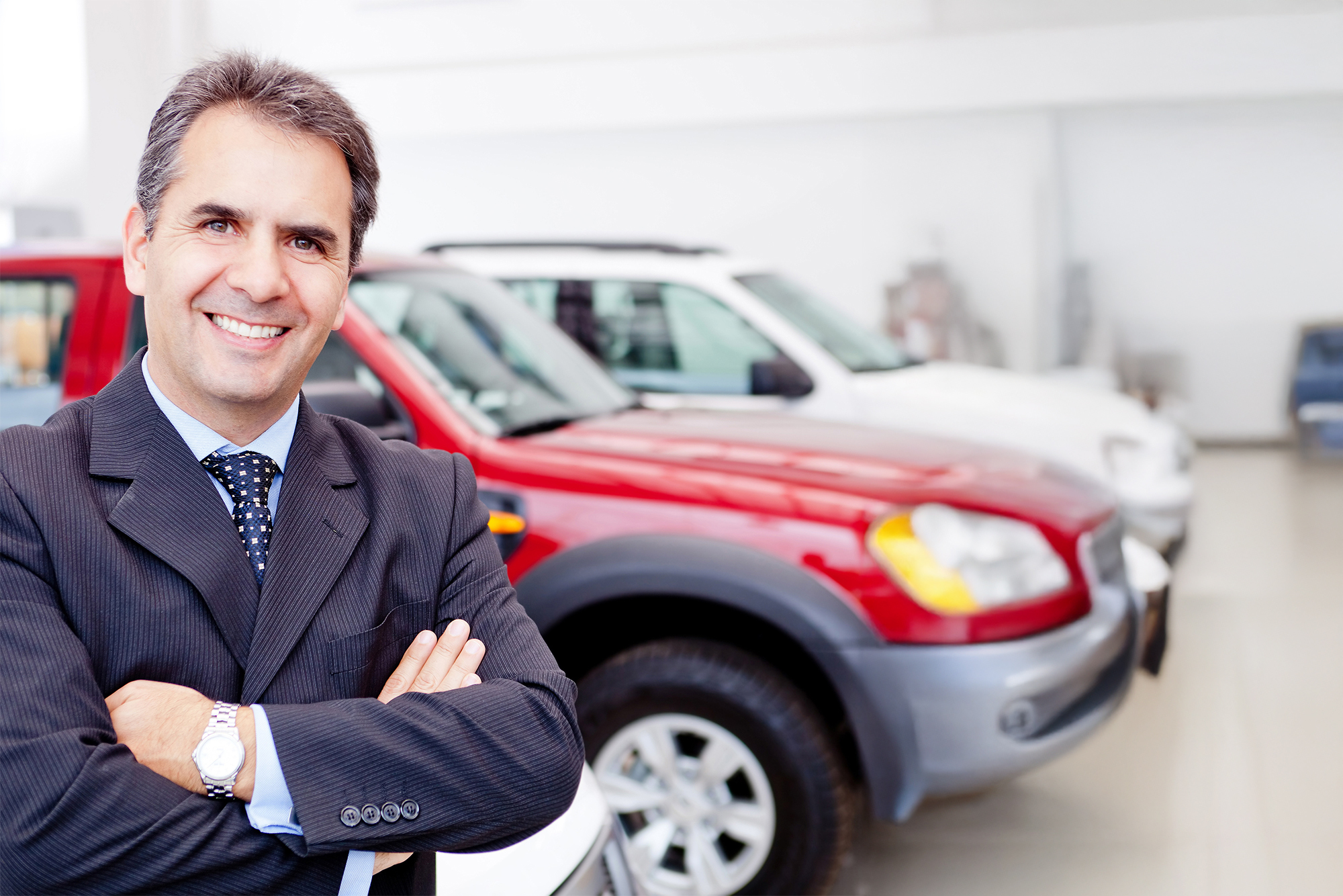 Salesman posing for a picture with a red car behind